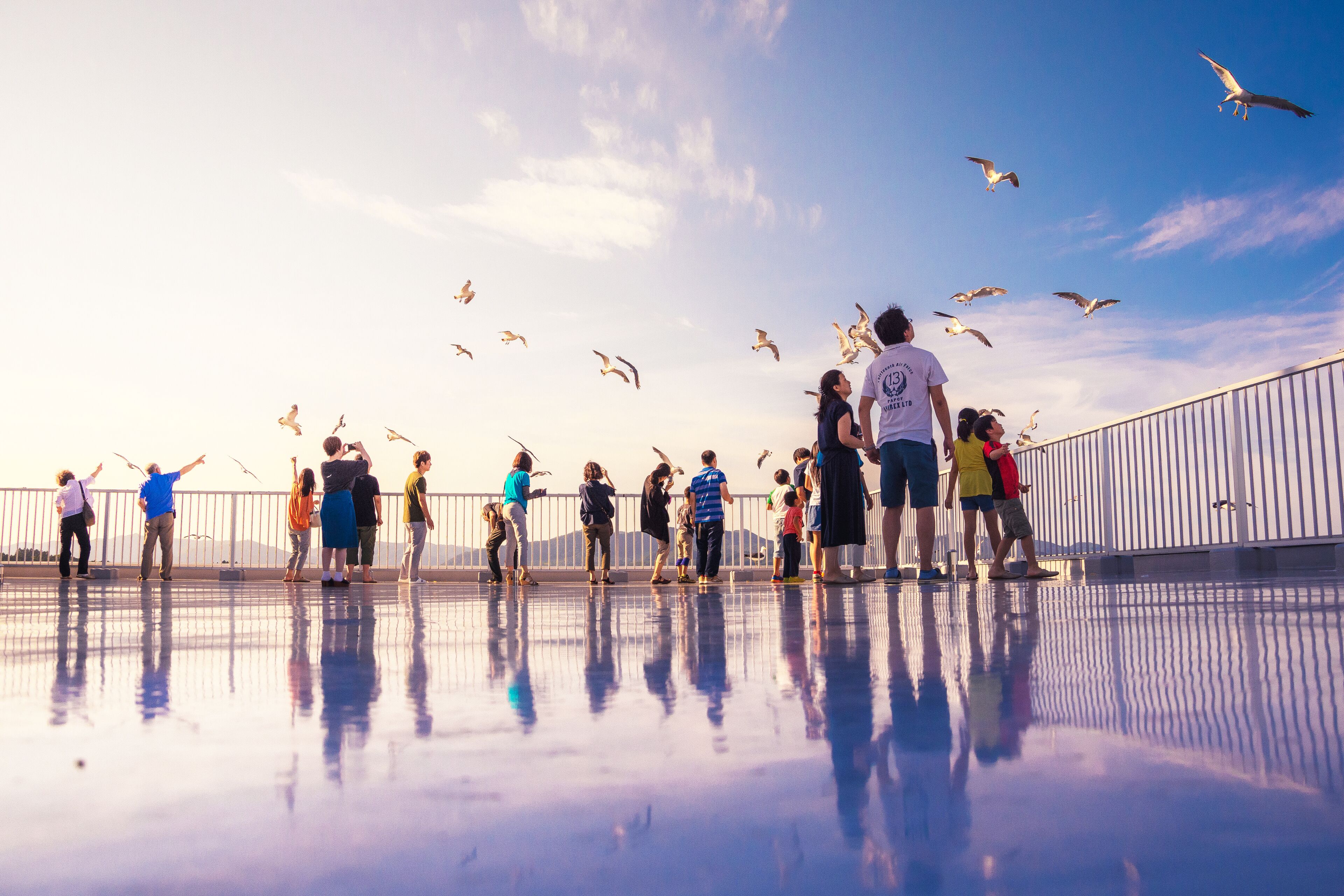 A group of people on a reflective surface with a railing and a clear sky.