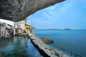 Un hotel costero con vistas despejadas al mar, un litoral rocoso y una escalera de piedra que conduce a la entrada.