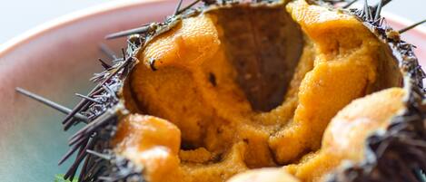 A close-up of a spiky, orange fruit with a hollow center, possibly a sea urchin, on a plate.
