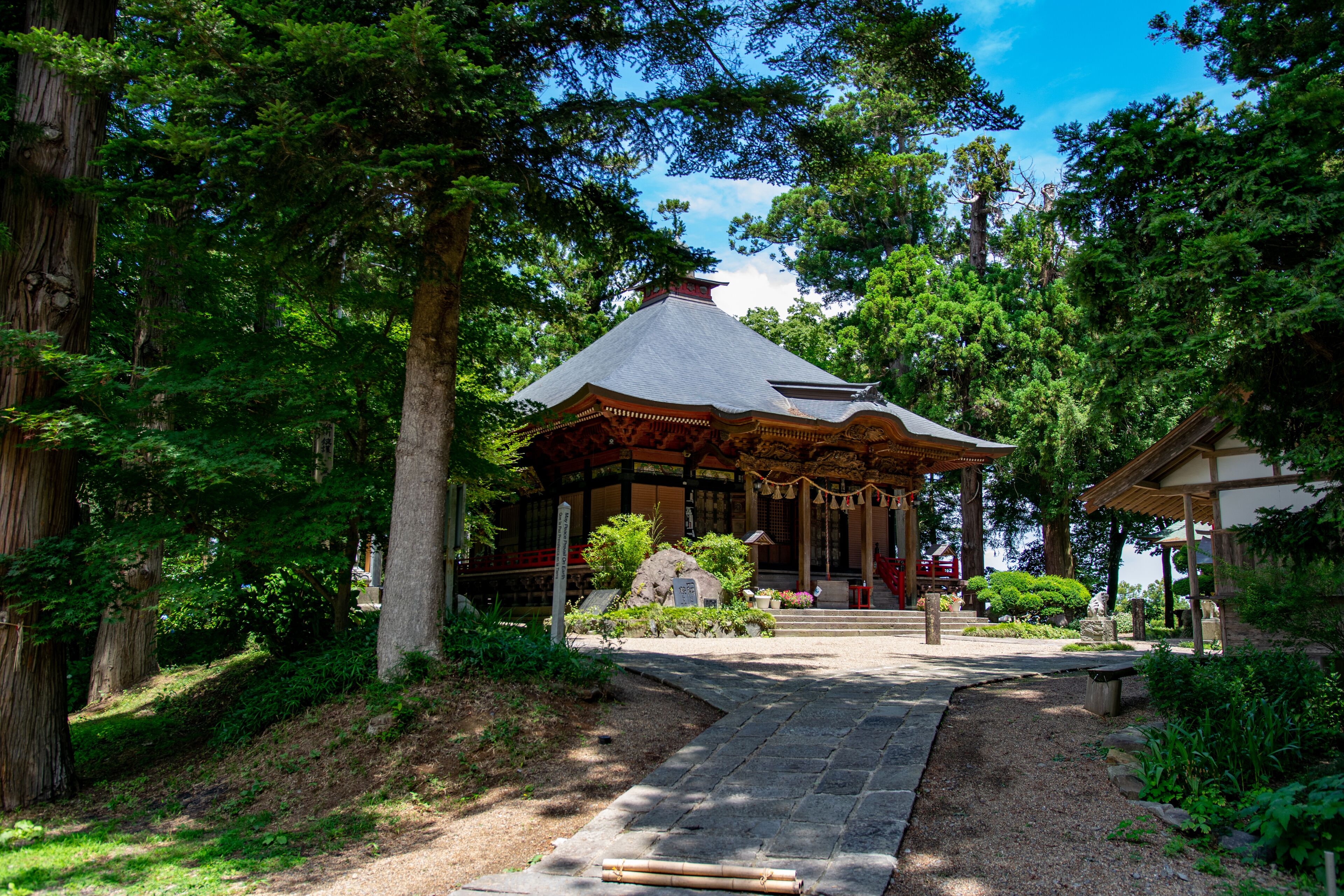 A traditional Japanese pavilion surrounded by lush greenery and a stone pathway leading to it.