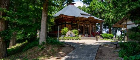 A traditional Japanese pavilion surrounded by lush greenery and a stone pathway leading to it.