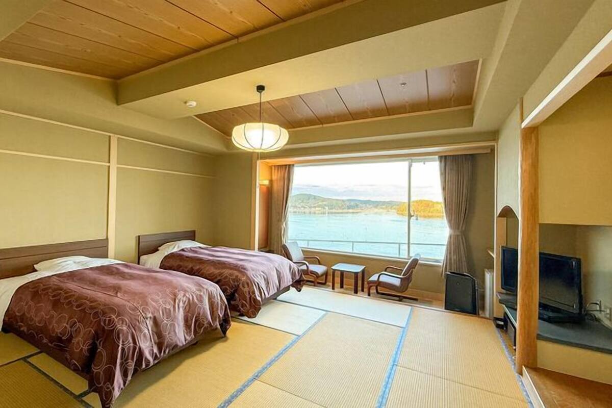A hotel room with two beds, a TV, a small table, and a view of the water.