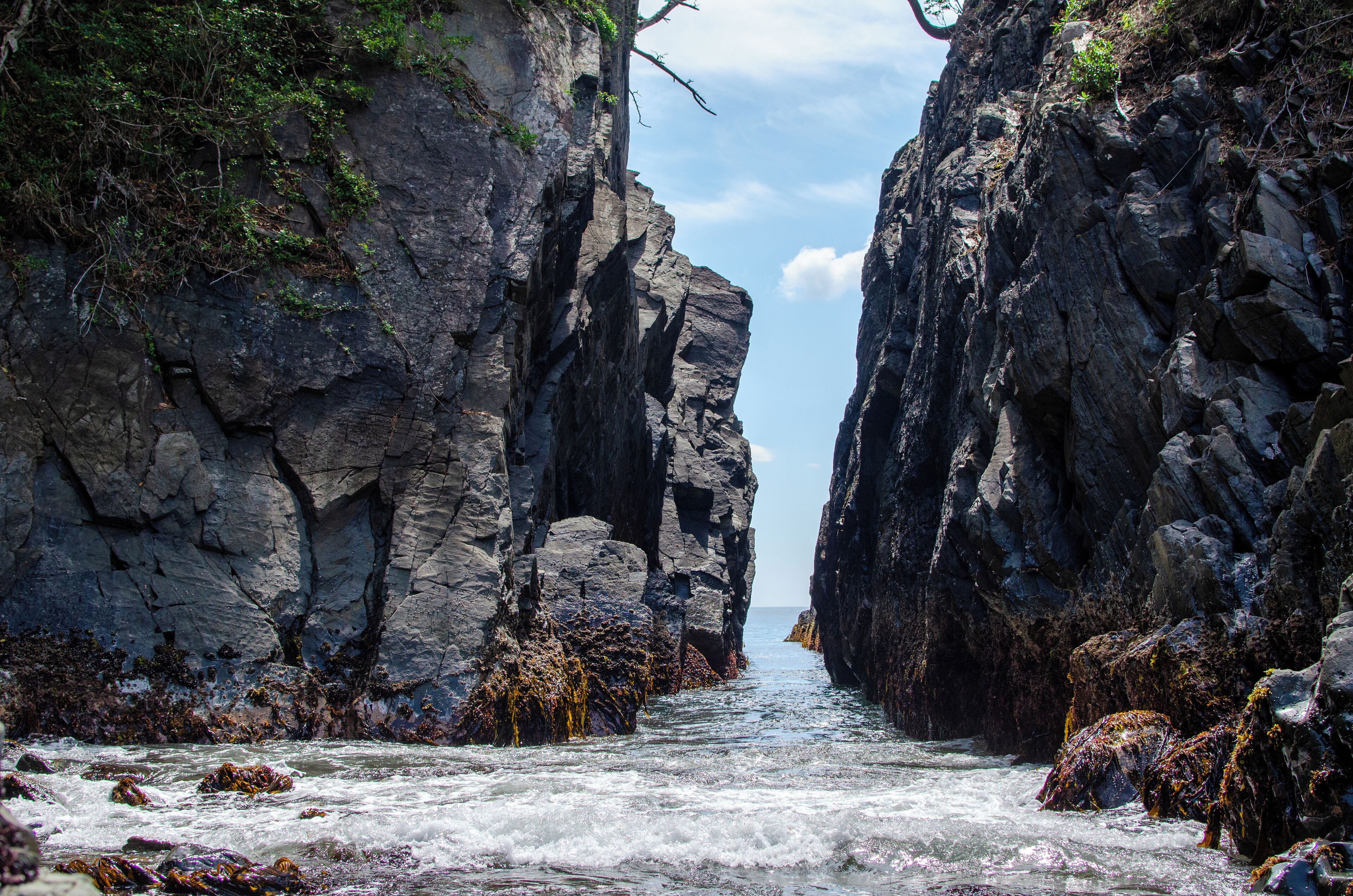 A rocky coastal landscape with a narrow passage between cliffs, leading to the sea.