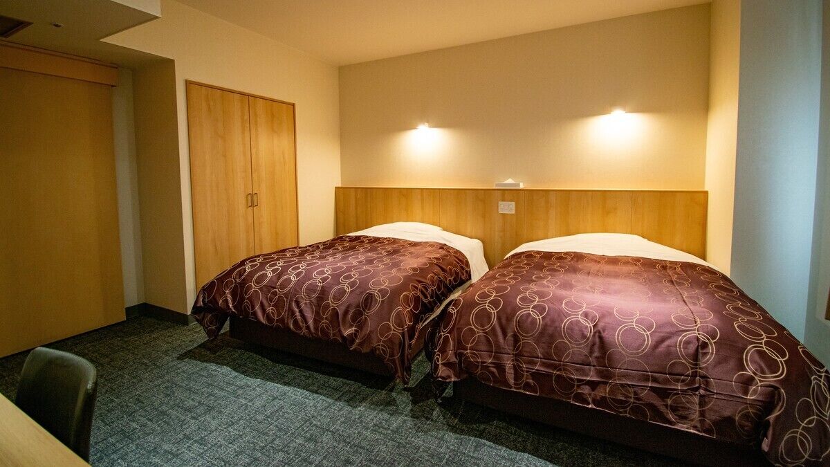 Una camera d'albergo con due letti, un armadio in legno e pavimento rivestito di moquette.