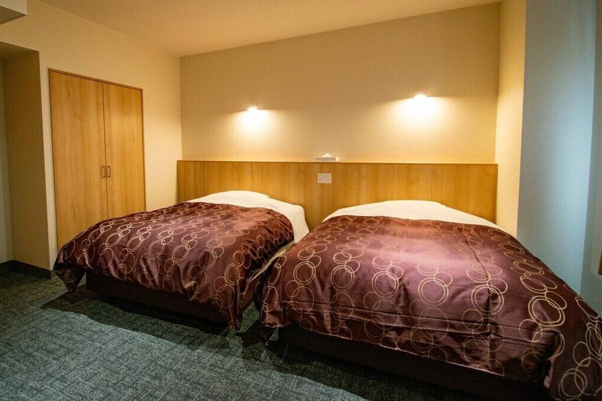 A hotel room with two beds, a wooden wardrobe, and a carpeted floor.