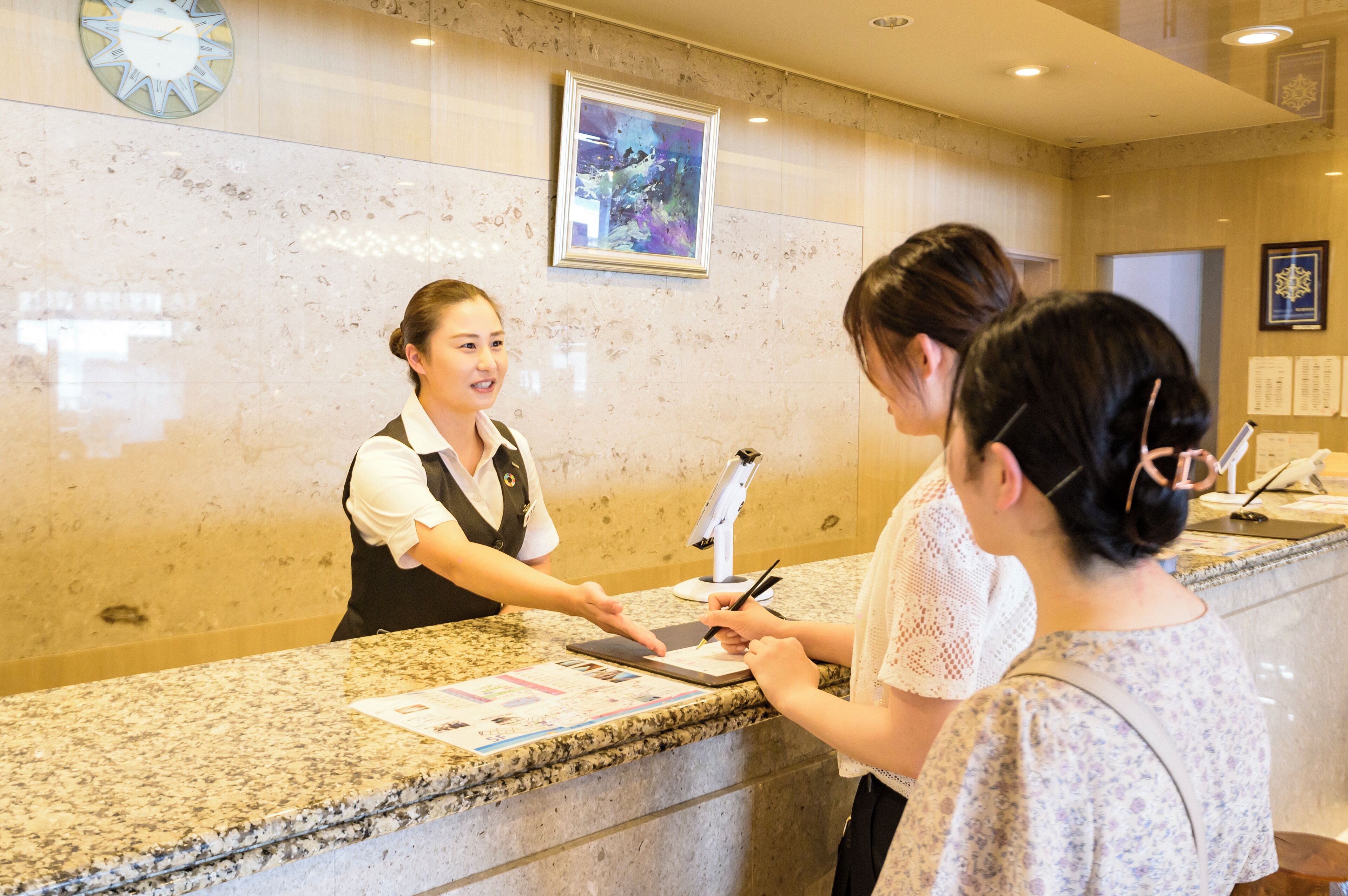 A reception desk with a receptionist, a clock, and a framed artwork on the wall.