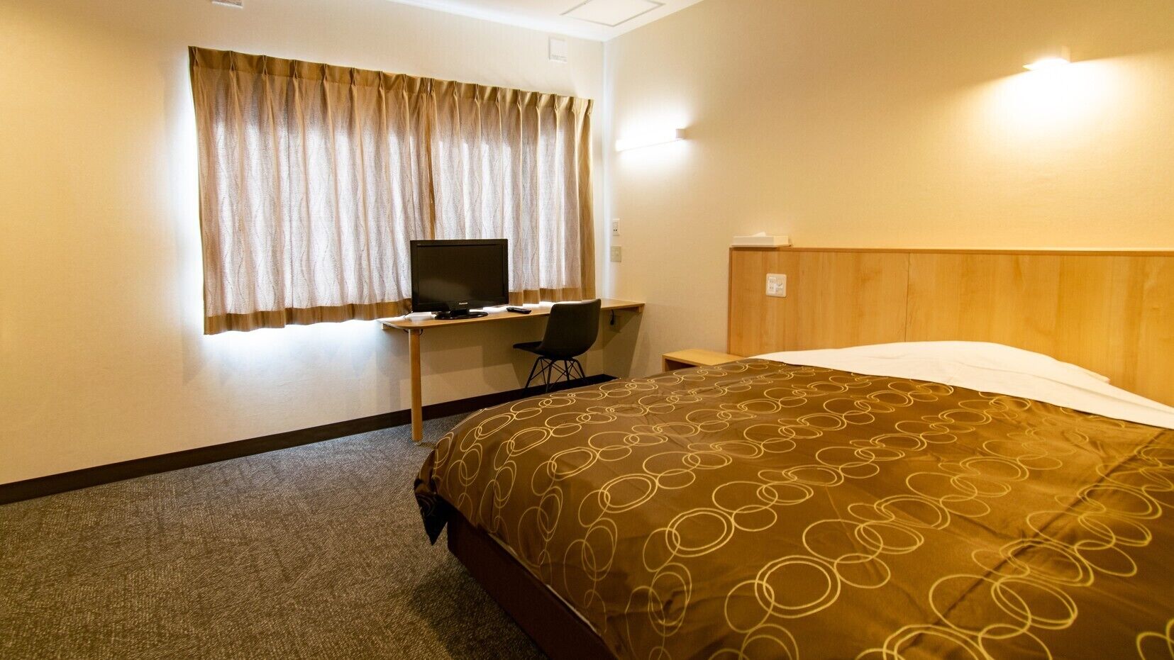 Una camera d'albergo con un letto, una scrivania con un computer, una sedia e una finestra con tende.