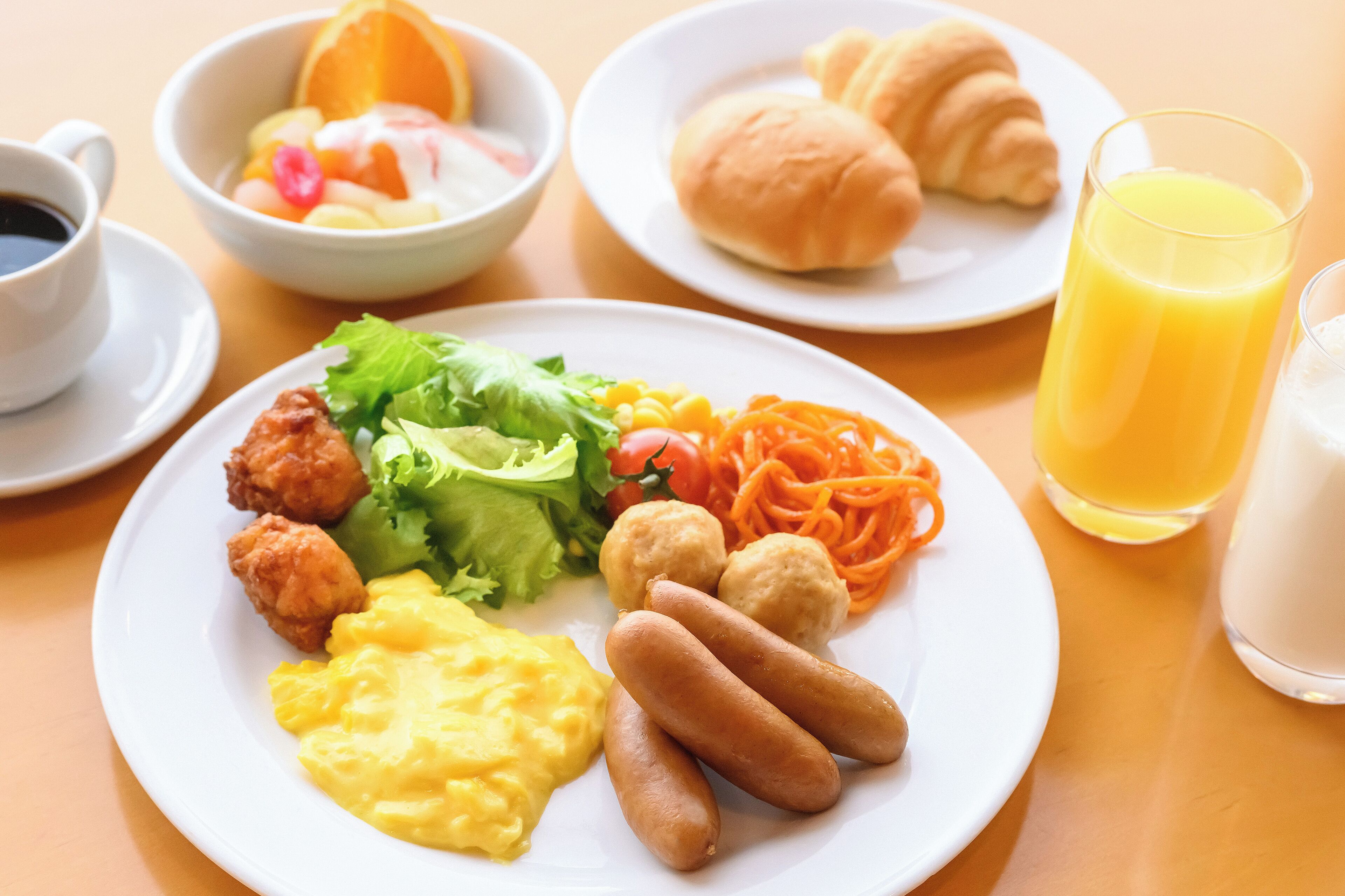 Une assiette de petit-déjeuner comprenant des œufs brouillés, des saucisses, une salade et un croissant.