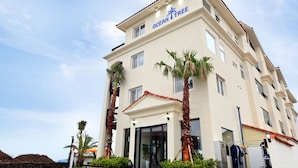 Ein mehrgeschossiges Hotel namens "Ocean Tree" mit einer beige farbenen Fassade, Palmen und blauem Himmel.