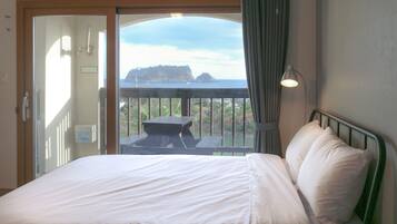 Una camera d'albergo con un letto, un comodino, una lampada e vista su un balcone con tavolo e sedie.