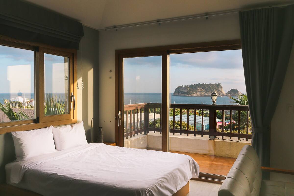 A hotel room with a bed, a balcony with a view of the sea, and a chair.