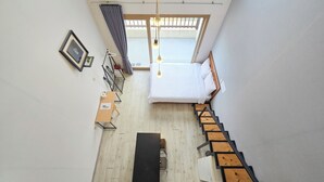 Ein Schlafzimmer mit einem Bett, einem Schreibtisch, einem Stuhl, einem Fenster mit Vorhängen und einer Treppe.