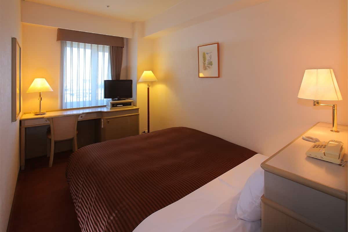 Une chambre d’hôtel équipée d’un lit, d’un bureau, d’une chaise, d’une télévision, de lampes et d’un téléphone.