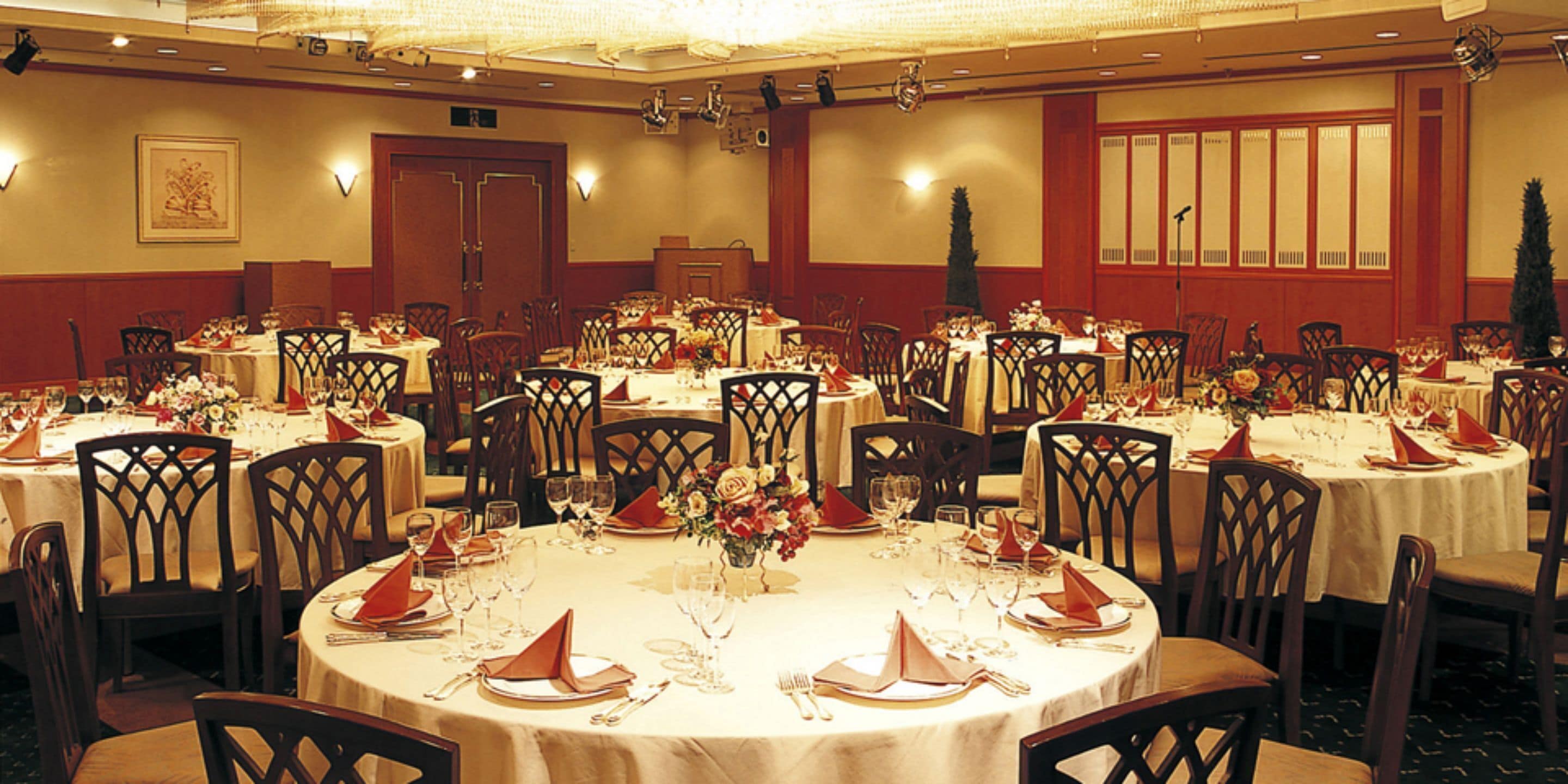 A banquet hall with multiple round tables set for dining, each with chairs and table settings.