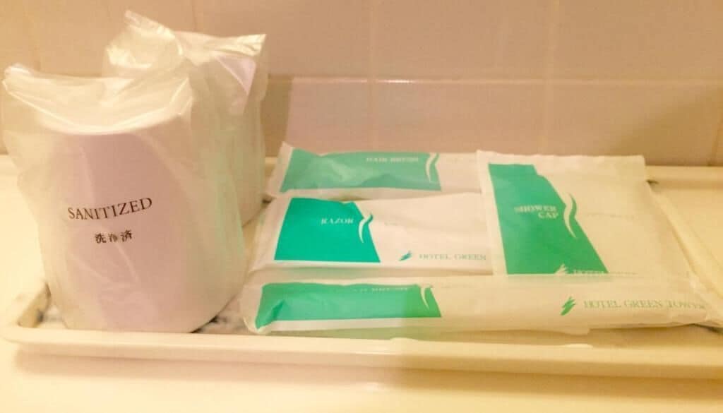 Tarjottimella on pussi, jossa on merkintä ”DESINFIOITU”, sekä useita paketteja, joissa on teksti ”HOTELIN VIHREÄT PYHKEET”.