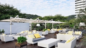 A deck with white wicker furniture, yellow cushions, and umbrellas providing shade.