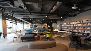 A modern cafe with a cozy seating area, a bookshelf, and a visible kitchen in the background.