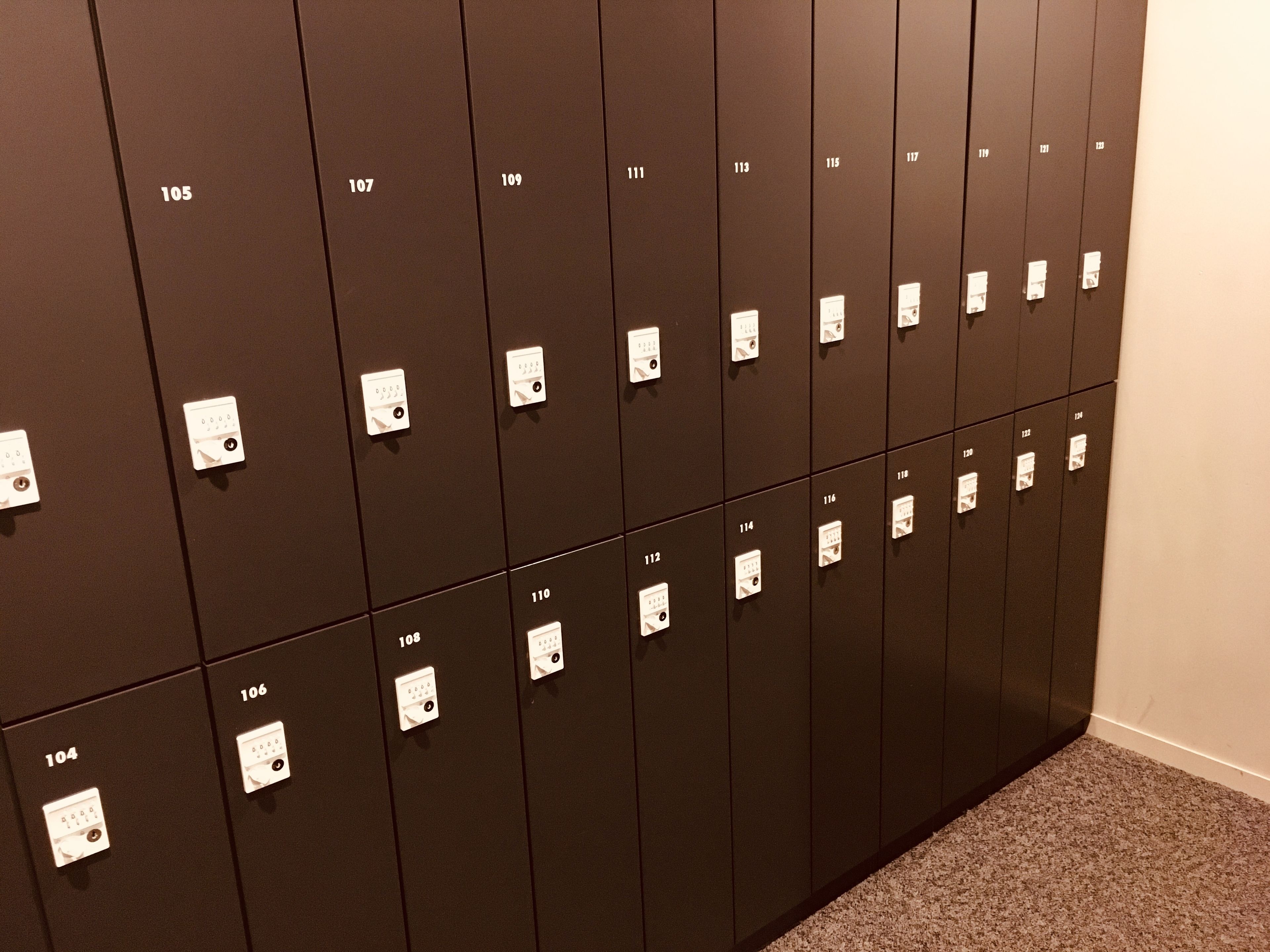A row of dark brown lockers with white numbers and lock mechanisms, arranged in a linear fashion along a wall.