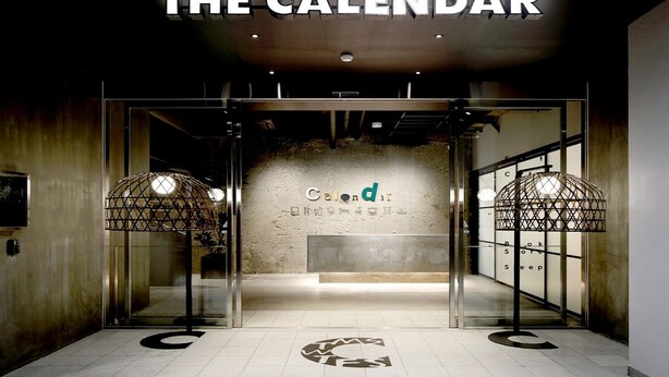The entrance to The Calendar hotel with a modern design, featuring a reception desk and two large, circular light fixtures.