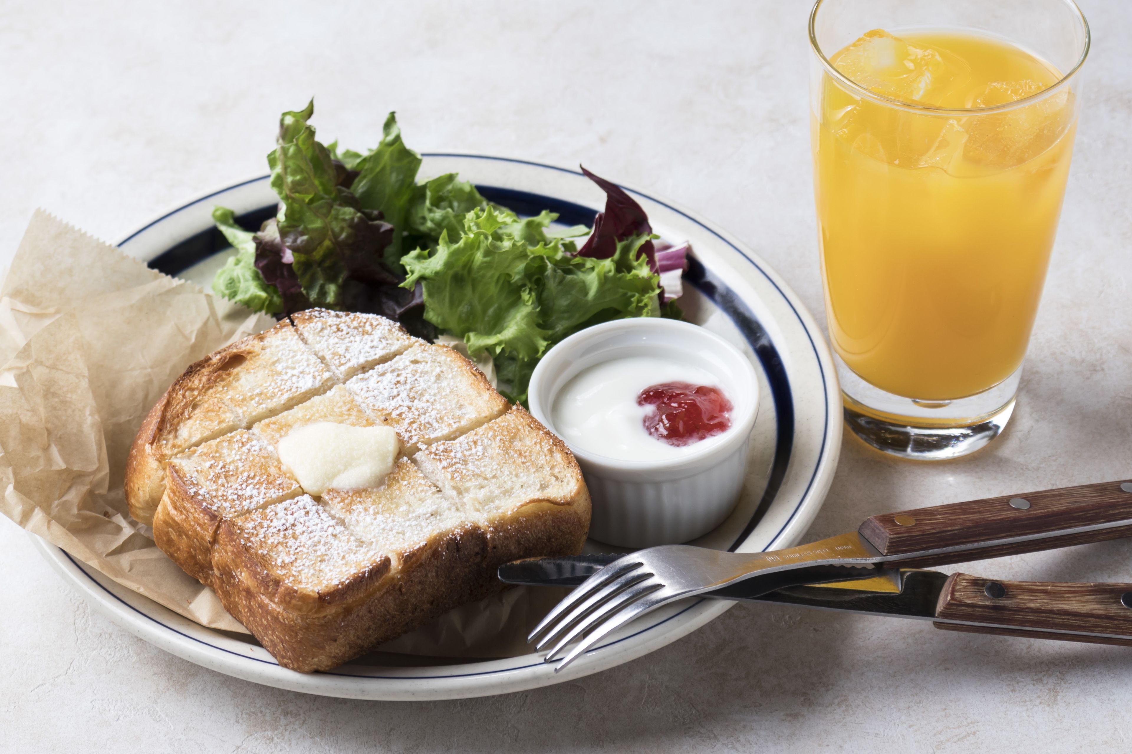 A plate with toast, a small bowl of jam, and a glass of orange juice.