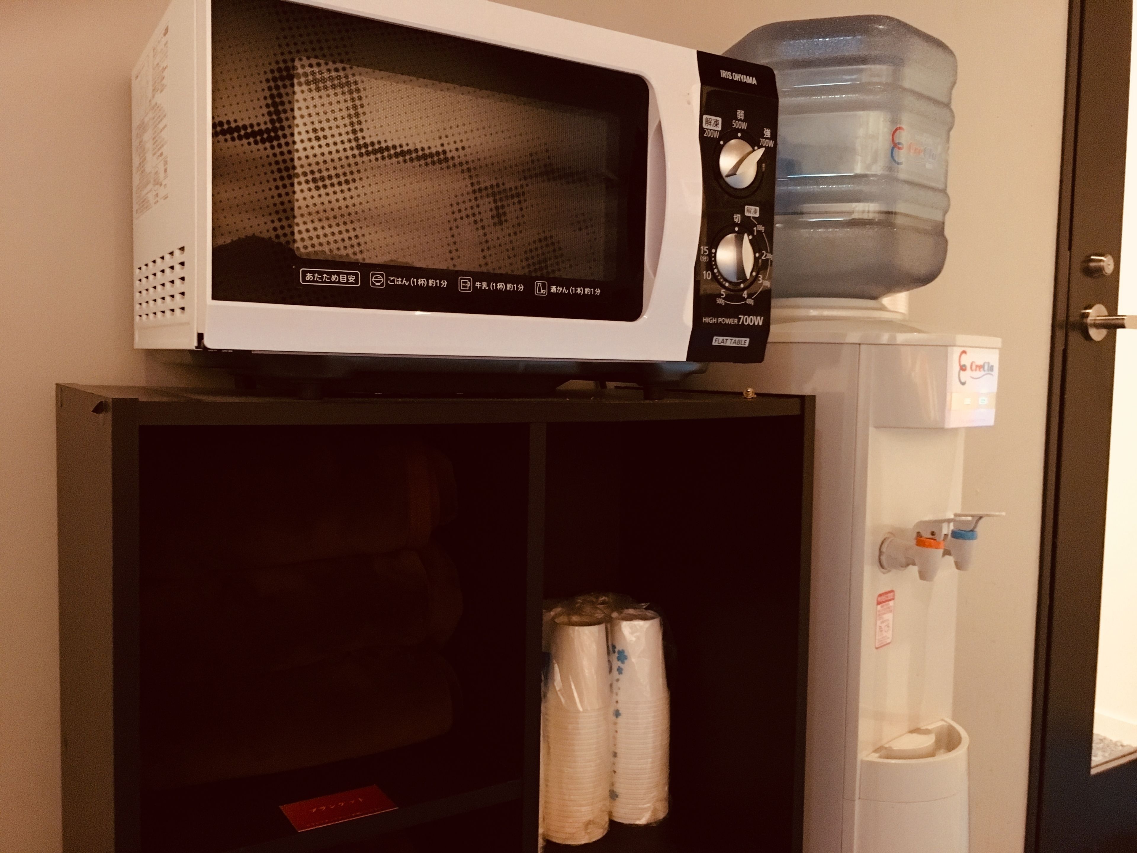 Un forno a microonde su un mobile, un dispenser di acqua e una TV a schermo piatto.