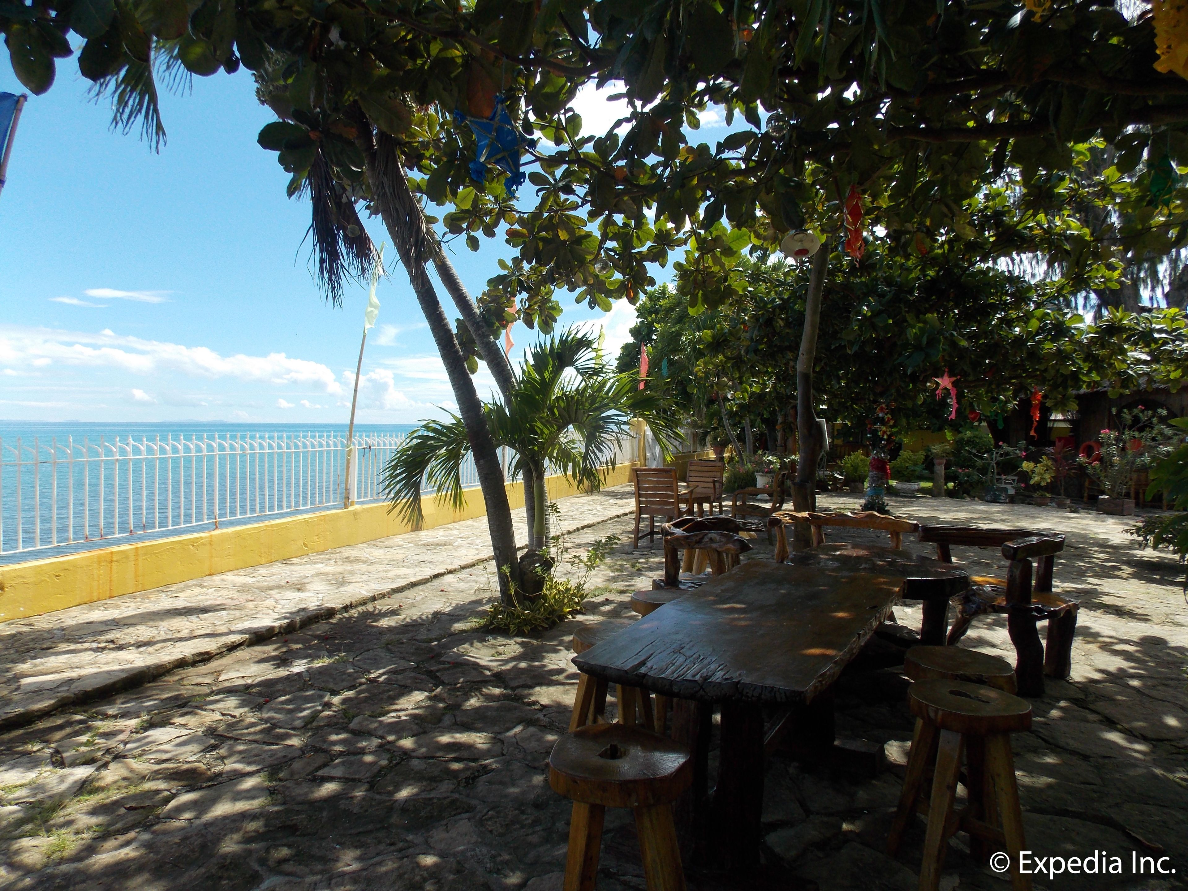 A beachside patio with a wooden table and chairs, a yellow railing, and a view of the sea.
