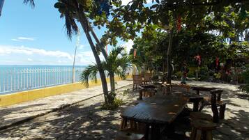 A beachside patio with a wooden table and chairs, a yellow railing, and a view of the sea.