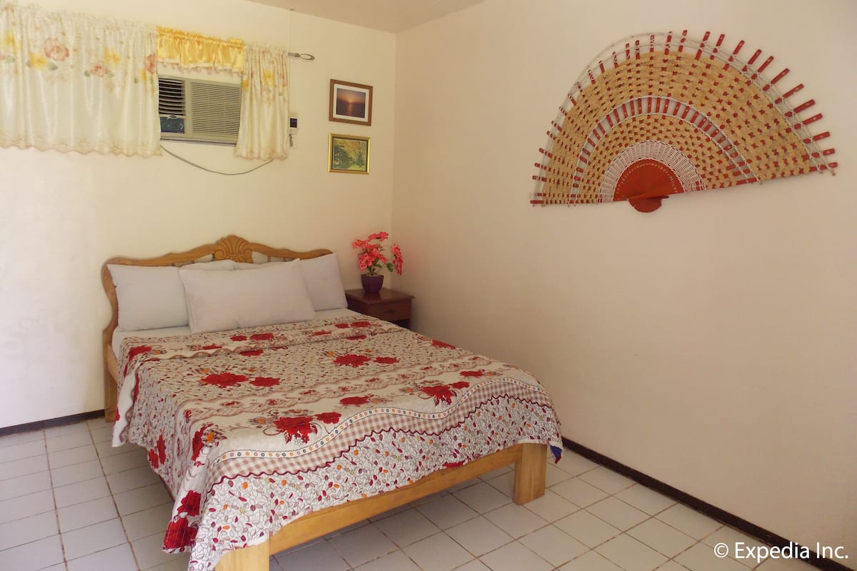 A bedroom with a bed, a nightstand, a wall-mounted fan, and a window with curtains.