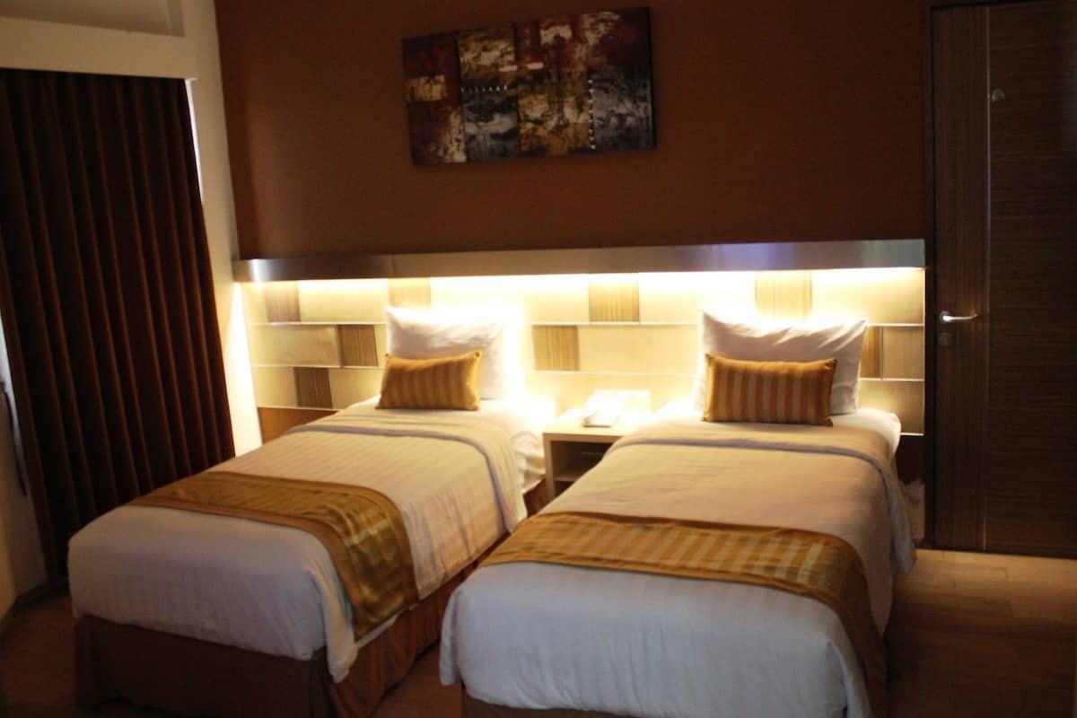 Une chambre d’hôtel avec deux lits, une tête de lit dotée d’un éclairage intégré, une table de chevet avec une lampe et un tableau accroché au mur.
