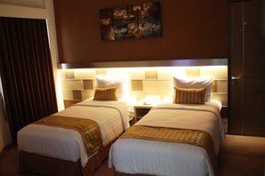 Habitación de hotel con dos camas, cabecero con iluminación integrada, mesita de noche con lámpara y un cuadro en la pared.