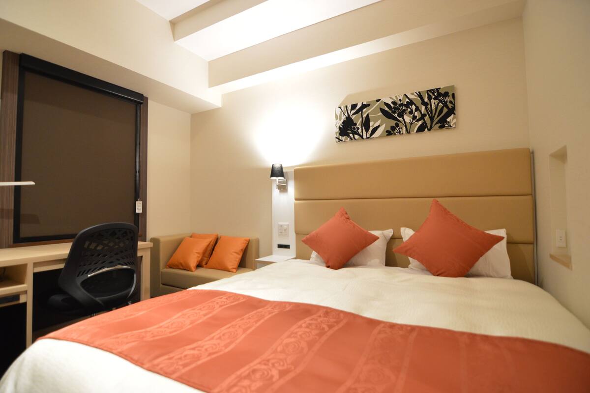 Una habitación de hotel con una cama, un escritorio, una silla y una mesita de noche.