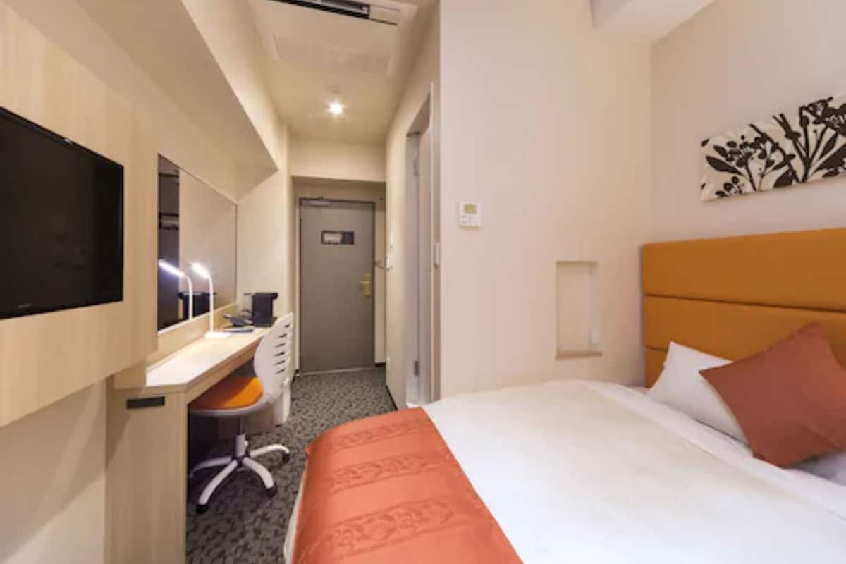 Una habitación de hotel con una cama, un escritorio con una silla, un televisor y una puerta que da a otra habitación.