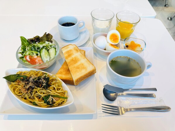 A table with a meal consisting of spaghetti, toast, a salad, a cup of coffee, a glass of juice, a boiled egg, and a cup of tea.