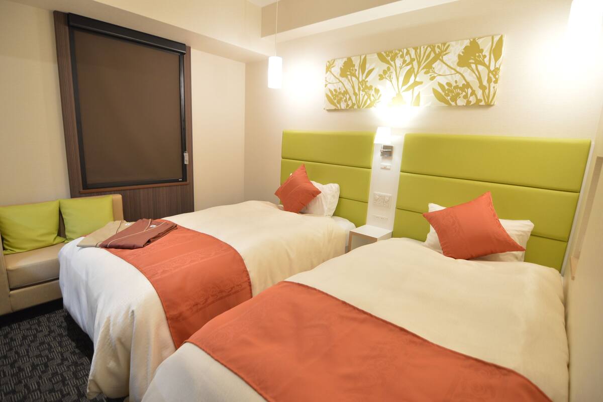 Habitación de hotel con dos camas, un sofá, un ventanal grande y una obra de arte colgada en la pared.