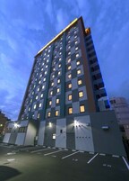 Um edifício alto com vários andares, cada um com várias janelas. O edifício tem um design arquitetônico moderno, com telhado plano e uma série de varandas. Há vagas de estacionamento em frente ao edifício.