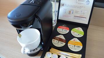 Une machine à café, une tasse et une boîte de différents mélanges de thé sont posés sur une table.