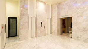 A modern hotel lobby with marble flooring, a glass elevator, and a reception desk. - Queen's Hotel Chitose (Chitose)