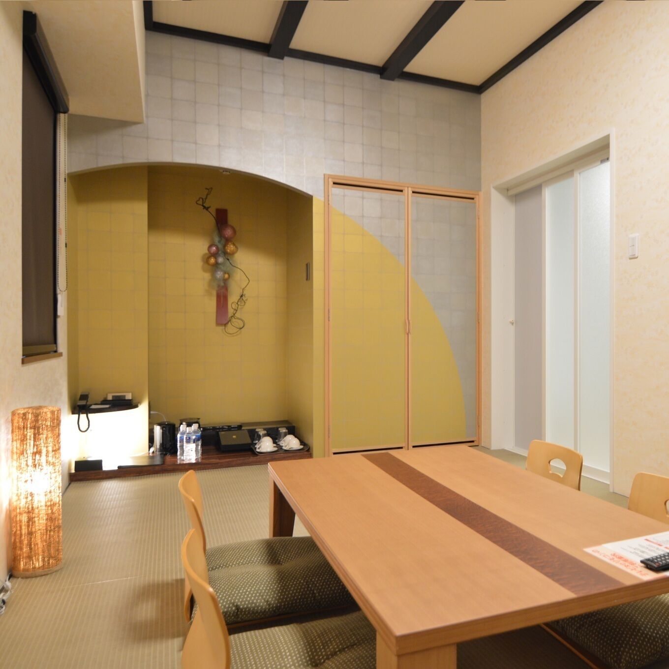 A hotel room with a wooden dining table, chairs, a small kitchenette, and a sliding door.
