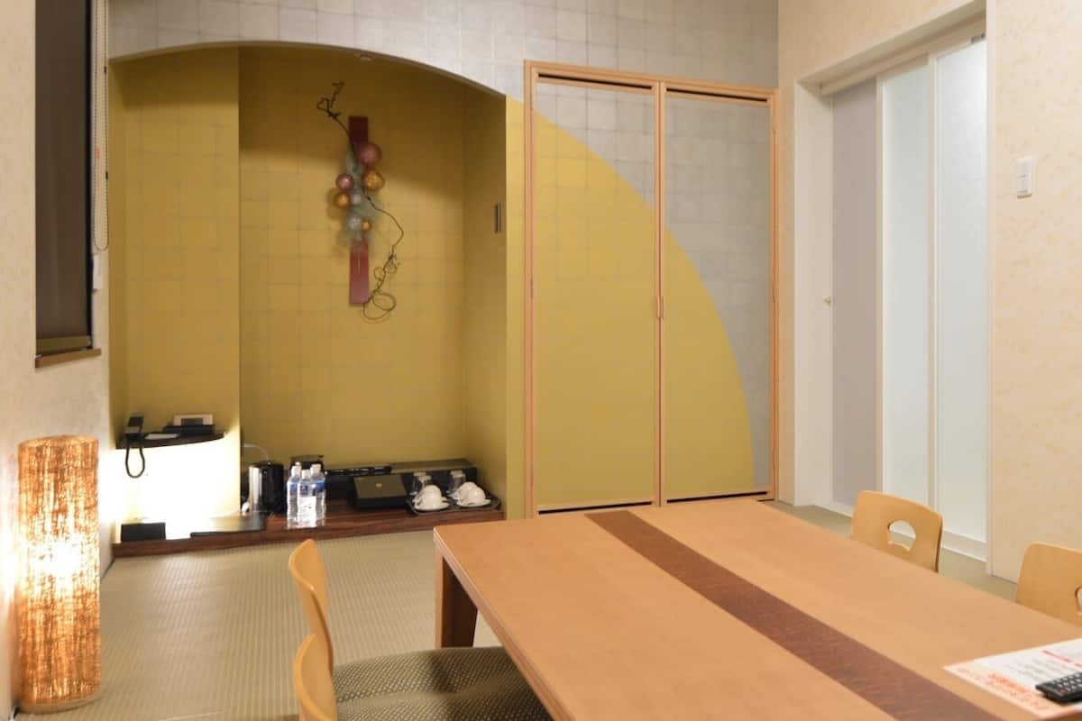Habitación de hotel con una mesa de comedor de madera, sillas, una pequeña kitchenette y una puerta corredera.