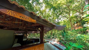 A reception area with a sign, wooden structure, and a pathway leading to a building surrounded by greenery. - Lost Resort (Rayong)