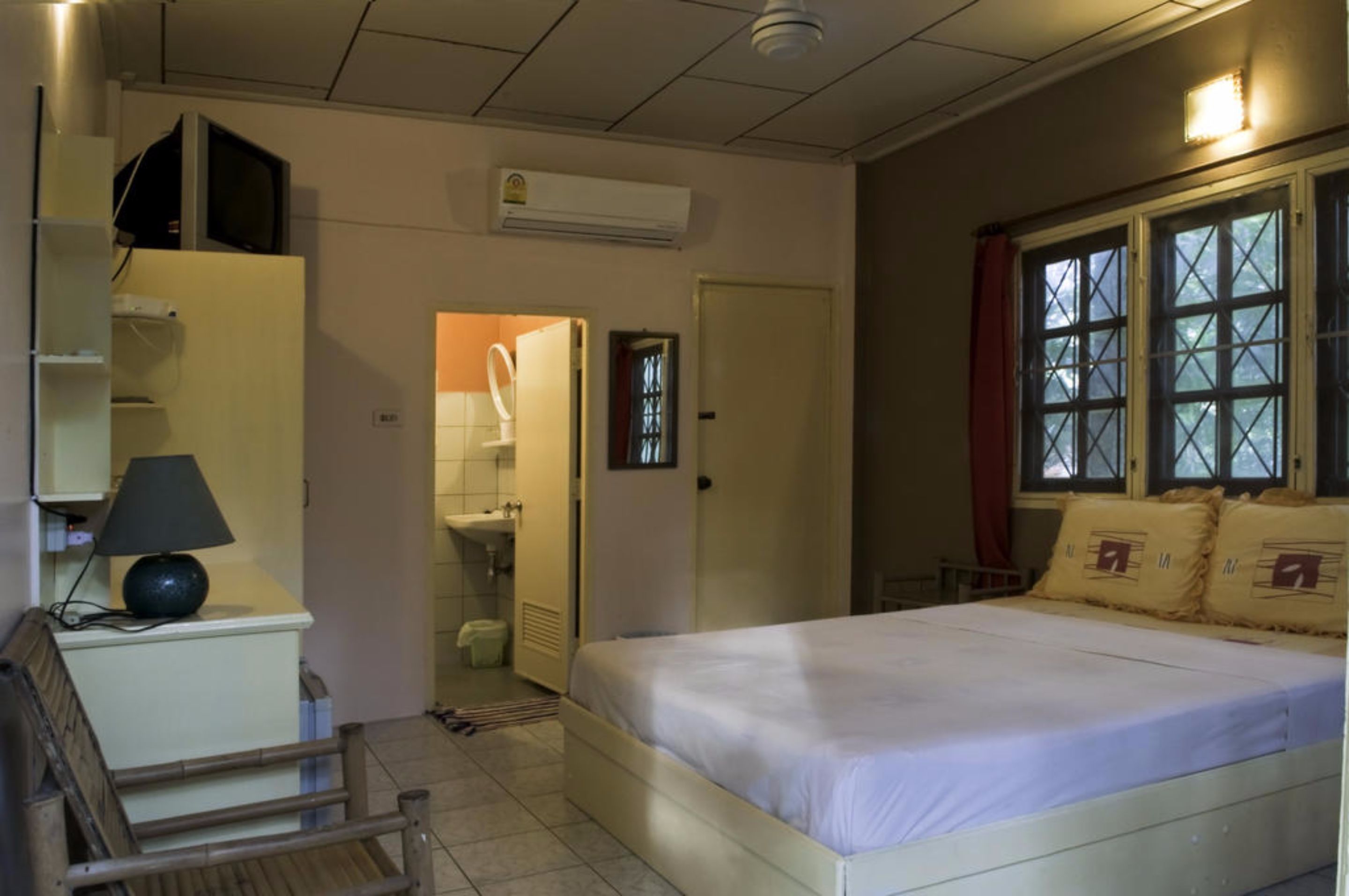 Un dormitorio con cama, escritorio con lámpara, armario y ventana con cortinas.