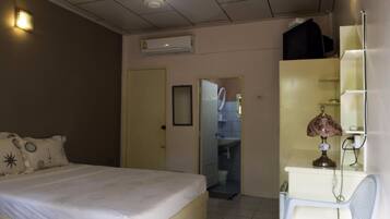 A hotel room with a bed, a desk with a lamp, a mirror, and an air conditioning unit.