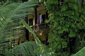Un edificio de dos pisos con balcones, rodeado de abundante follaje.