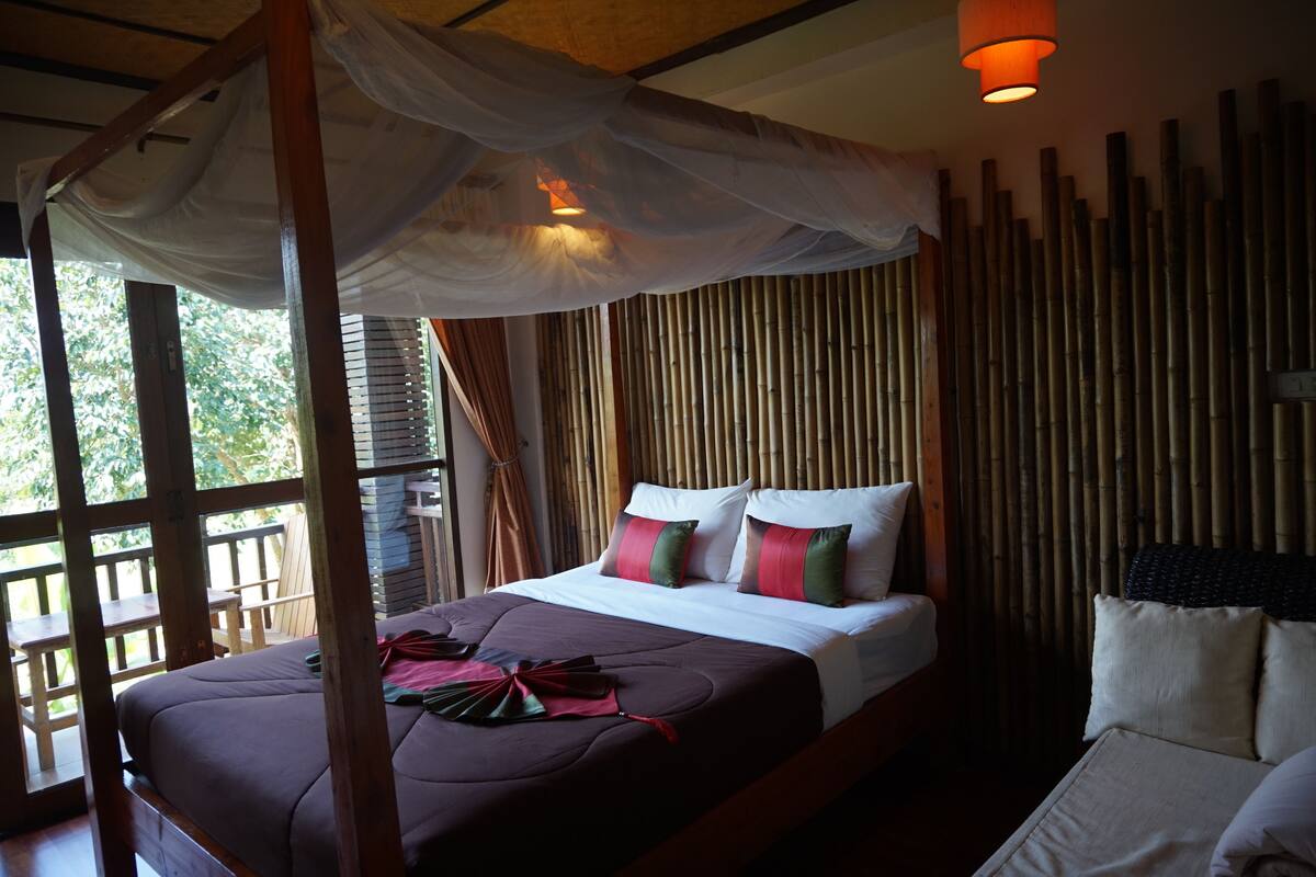 A bed with a canopy, a wooden headboard, and a view of bamboo walls.