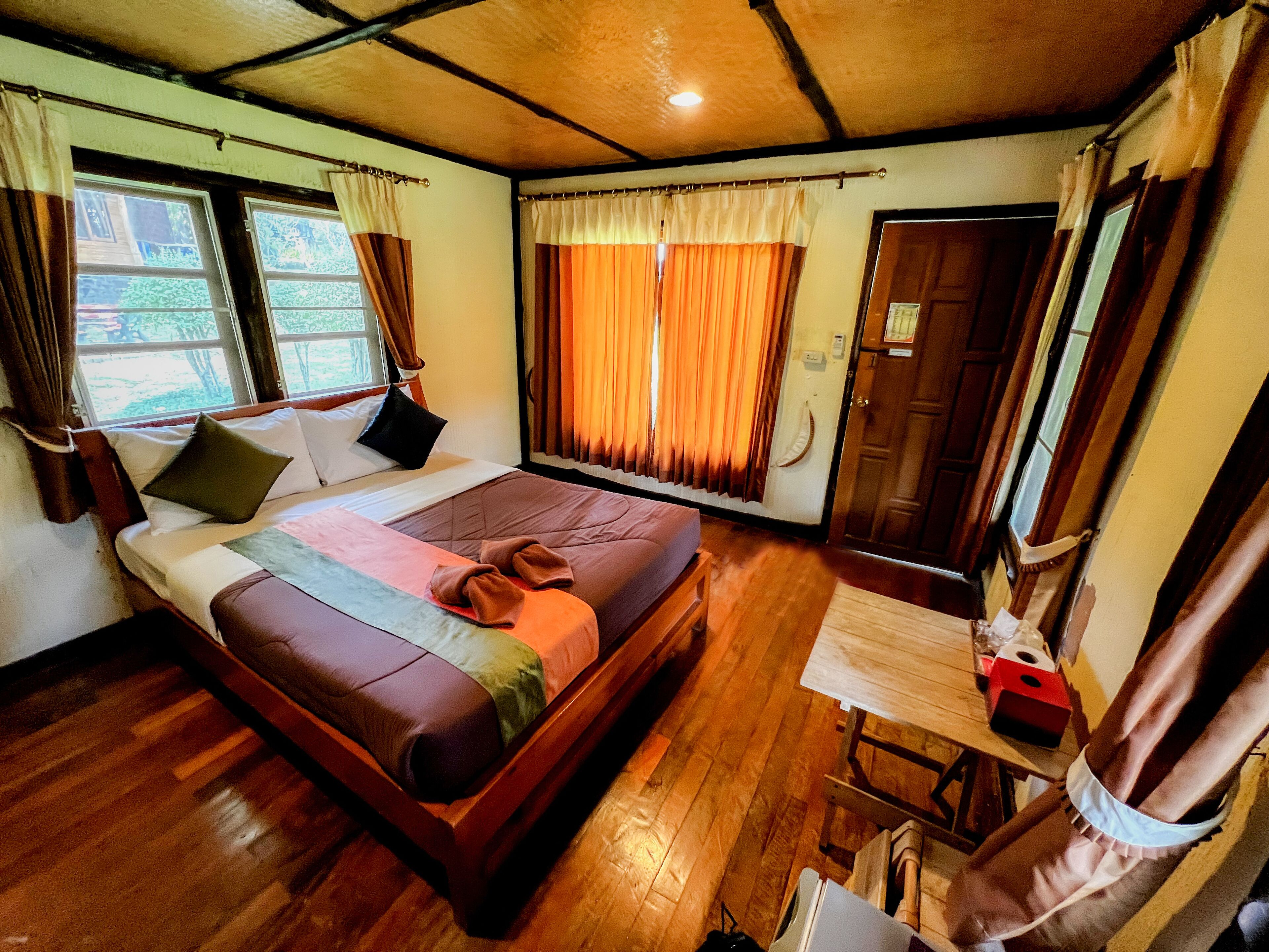 Una habitación con cama, suelo de madera, una mesita y cortinas.