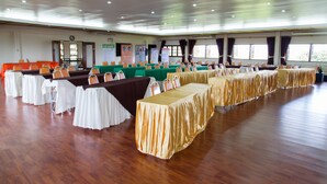 Un salón de conferencias con varias mesas y sillas, suelo de madera y amplios ventanales.
