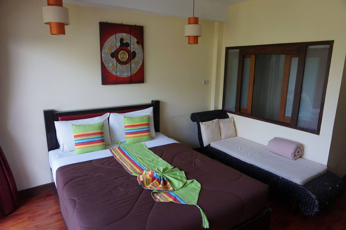 A hotel room with a large bed, a smaller sofa bed, a window with blinds, and a decorative wall piece.
