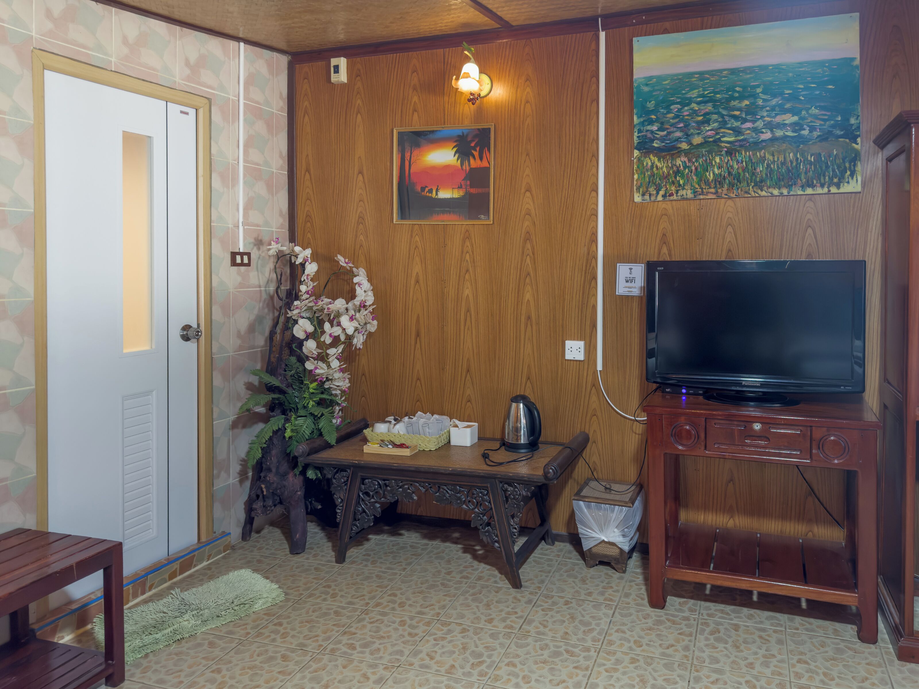 Una habitación con pared de madera, televisor, una mesa con una planta y una puerta.