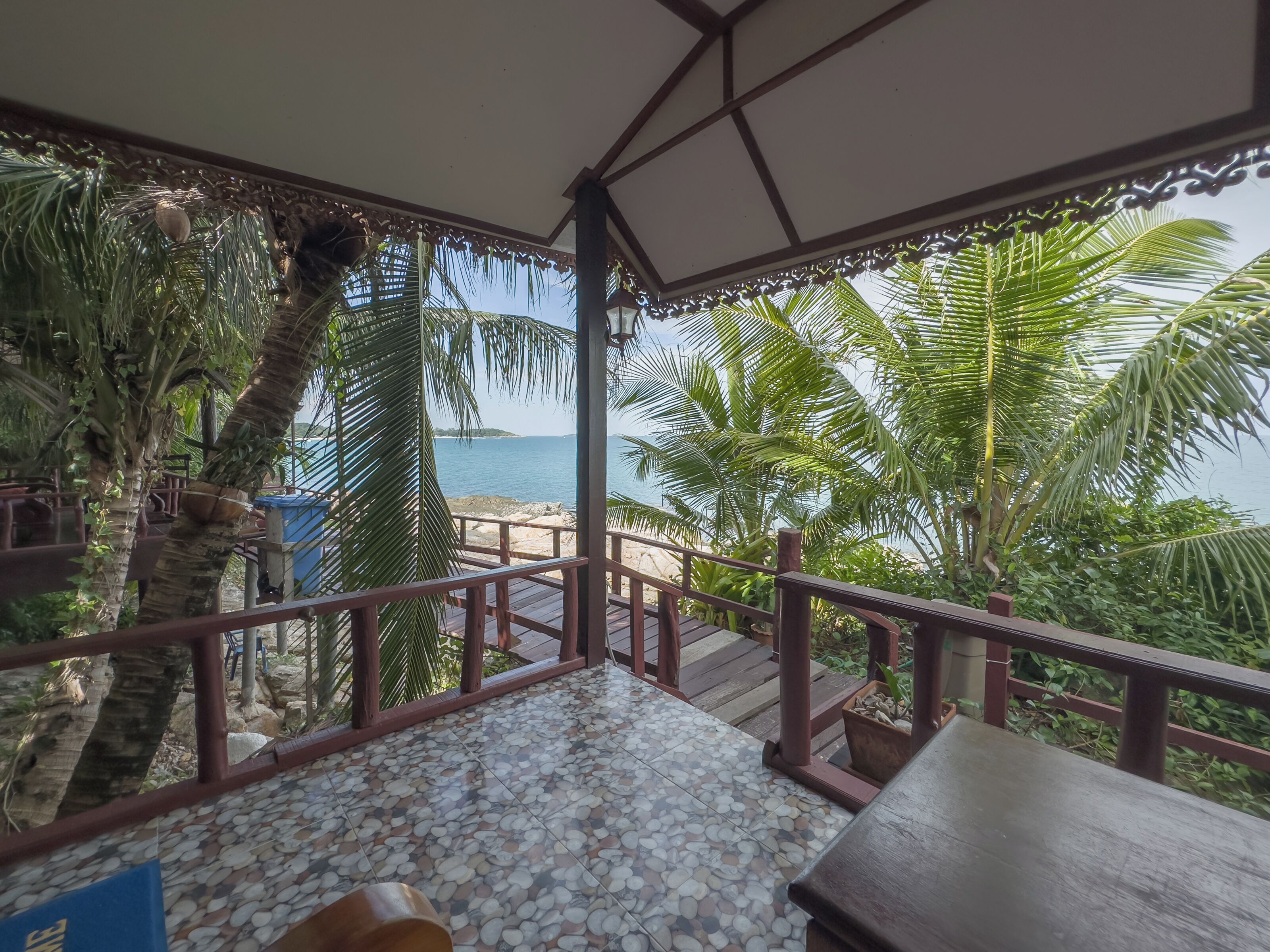 A covered outdoor area with a tiled floor, wooden railing, and a view of the sea.