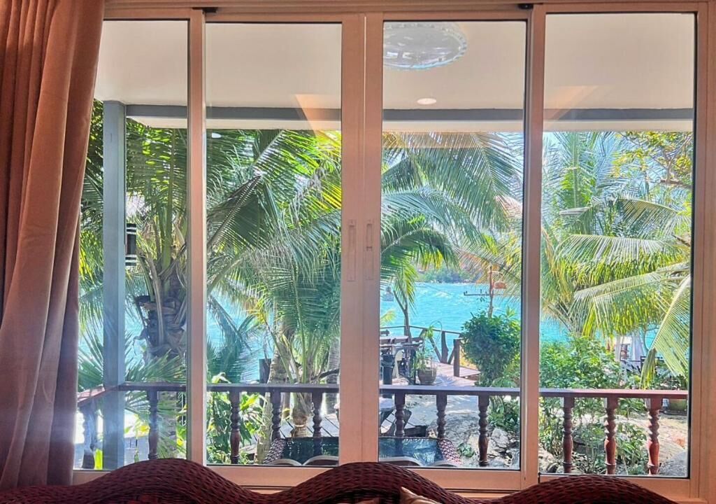 A room with a view of a tropical landscape through large sliding glass doors.